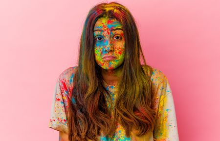Woman with Holi colours on her face and an upset expression looking at her hair